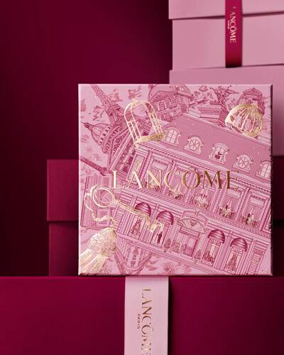 Elegancki stos rożowych i głęboko bordowych pudełek z Lancome, z centralnym pudełkiem ozdobionym złotymi paryskimi ilustracjami architektonicznymi.