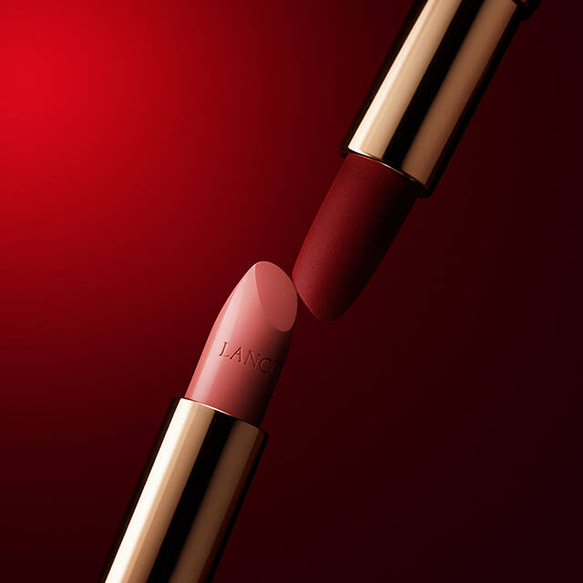 A close-up of two lipstick tubes with gold accents against a red background, one in a bold red shade and the other in a soft pink shade.