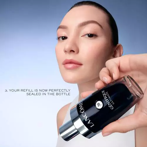 Młoda kobieta trzyma butelkę serum Lancome, uśmiechając się z zadowoleniem na tle jasnego nieba.