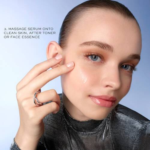 Młoda kobieta aplikuje serum na twarz, trzymając palec przy skorze. Ekspozycja na błyszczącej, niebieskiej tle.