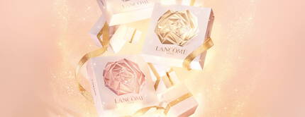 Zarowno luksusowe opakowania kosmetykow Lancome, jak i rożowe i złote wstążki na tle pastelowego koloru, tworzą elegancką kompozycję.