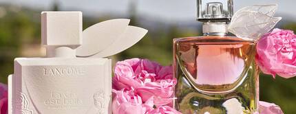 Dwa flakony perfum Lancome otoczone rożowymi rożami na tle jasnego nieba.