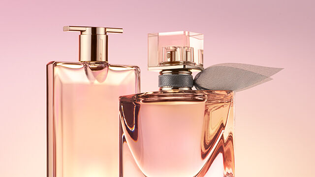 Two elegant perfume bottles are displayed against a soft pink background. One bottle has a sleek, rectangular shape, while the other is more rounded and adorned with a decorative element.