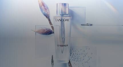 Butelka serum Lancome Clarifique na tle z delikatnymi gałązkami i kroplami wody.