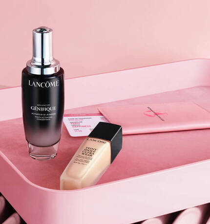 A bottle of Lancome Advanced Genifique serum and a tube of Lancome foundation displayed on a pink fabric background, with a soft, elegant setting.