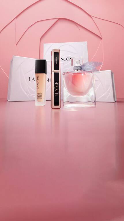 Obraz przedstawia produkty kosmetyczne marki Lancome na rożowym tle, w tym flakon perfum oraz podkład w eleganckich opakowaniach.