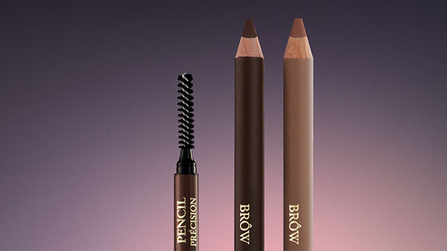 A close-up of two eyebrow pencils and a spoolie brush against a gradient background, showcasing different shades of brown.
