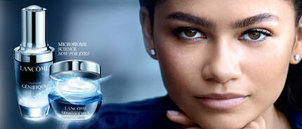 A close-up of a woman with dark hair and earrings, featuring skincare products from Lancome, including a serum and a cream, against a dark blue background.