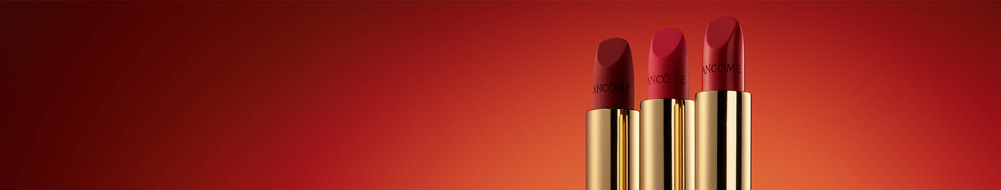 Three red lipsticks with golden packaging arranged side by side against a gradient orange background.