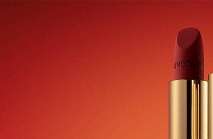 Three red lipsticks with golden packaging arranged side by side against a gradient orange background.