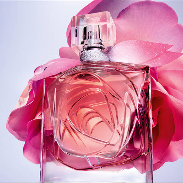 A bottle of perfume surrounded by soft pink rose petals, set against a gradient background. The bottle is elegantly designed, reflecting light and showcasing the fragrance inside.