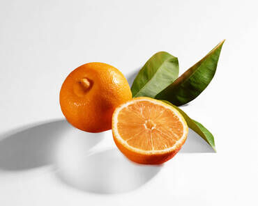 A whole orange and a sliced orange half, accompanied by green leaves, set against a white background.