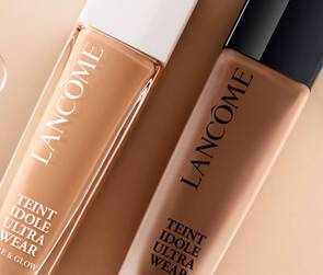 Dwa flakony podkładu Lancome Teint Idole Ultra Wear na jasnym tle, otoczone kroplami wody.