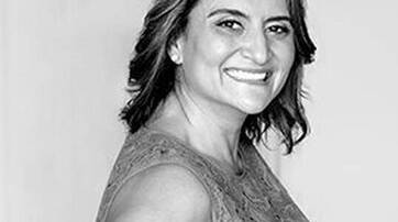 A smiling woman with shoulder-length hair, wearing a sleeveless dress, poses against a light background.