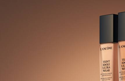 Three bottles of Lancome foundation in various shades, elegantly displayed against a warm, gradient background.