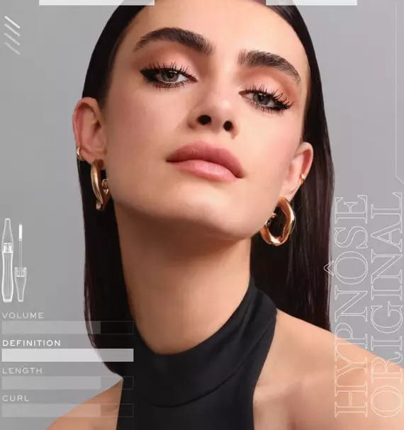 A close-up image of a woman showcasing flawless makeup, with emphasis on her defined eyelashes and smooth skin. She has dark, straight hair and is wearing bold earrings. The text on the side highlights features related to mascara, such as volume and definition.