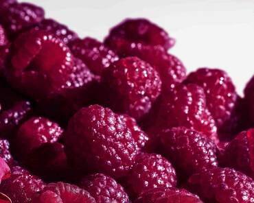 A close-up image of plump, vibrant raspberries with a glossy surface, arranged closely together.