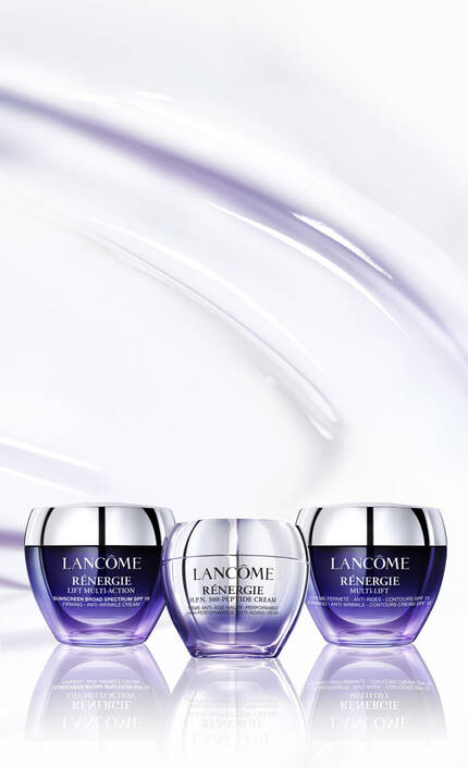 Three jars of Lancome Renergie skincare products are displayed against a soft, flowing purple background. The jars are elegantly shaped, with labels indicating “Multi-Action,” “Moisture Cream,” and “Multi-Lift.”