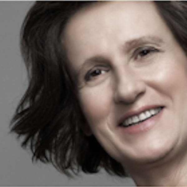 A woman with short, wavy dark hair smiling at the camera against a grey background.