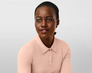 A woman with dark skin and a smooth bun hairstyle smiles softly while wearing a light pink collared shirt. The background is a subtle gradient of grey.