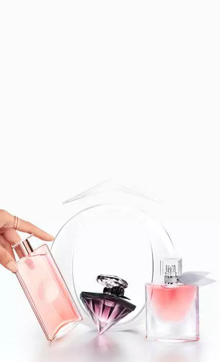 A hand reaching for a pink perfume bottle beside two other elegant perfume bottles against a light pastel background.