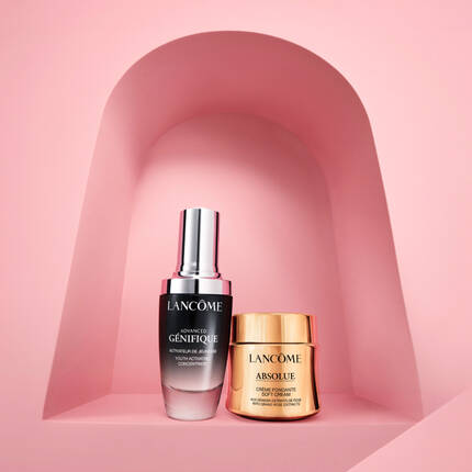 Dwa produkty kosmetyczne marki Lancome: serum Advanced Genifique i krem Absolue, umieszczone na rożowym tle w formie łuku.