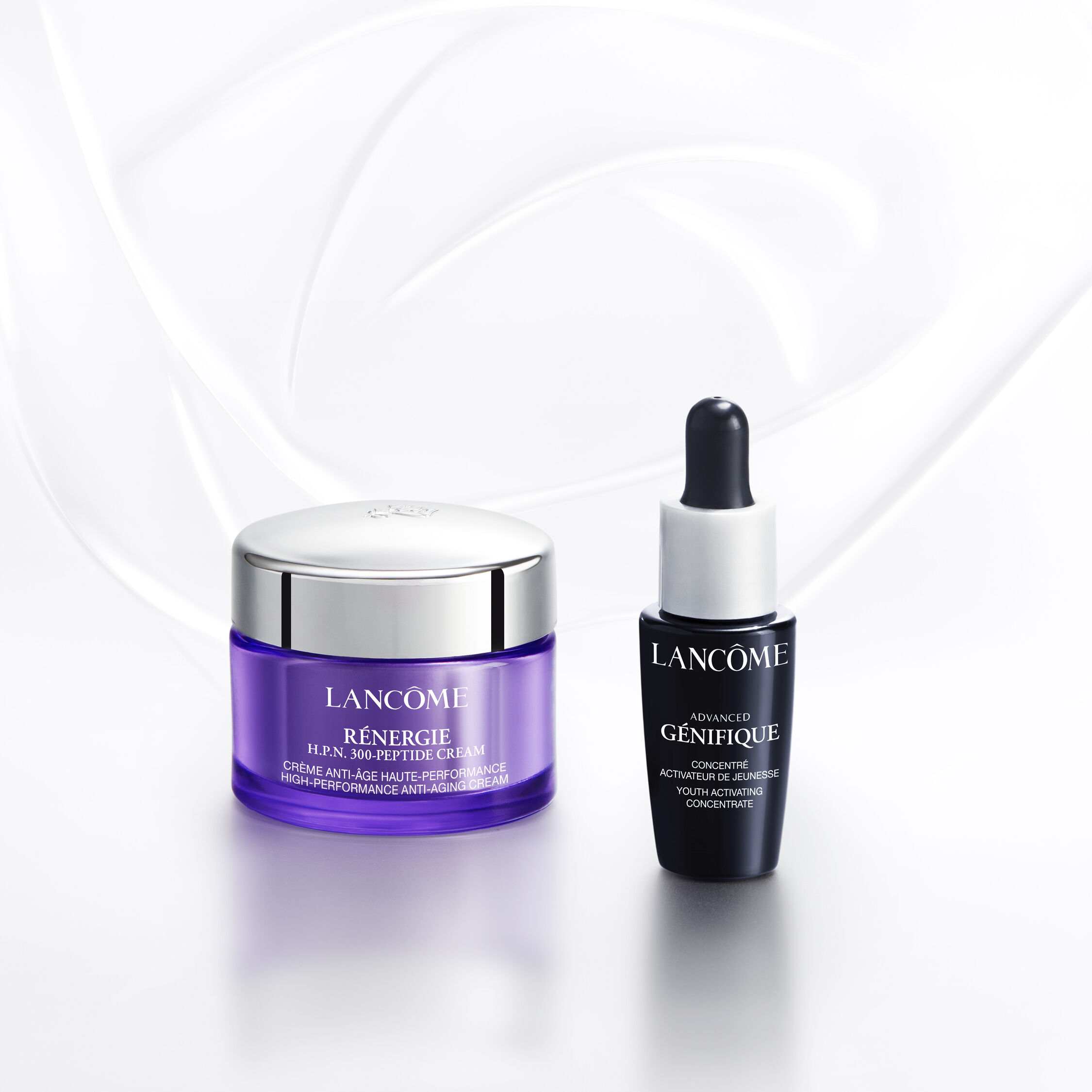 Text alternativ: Imaginea prezintă diverse produse cosmetice Lancome, inclusiv parfumuri, seruri, și un ruj, aranjate pe un fundal alb. Mainile interacționează cu unele dintre produse.