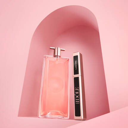 Na rożowym tle znajdują się dwa produkty kosmetyczne: flakon z rożowym perfumem i tusz do rzęs marki Lancome.