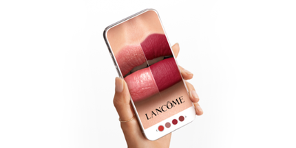 Smartfon w dłoni z aplikacją pokazującą cztery rożne odcienie szminki marki Lancome na ustach.