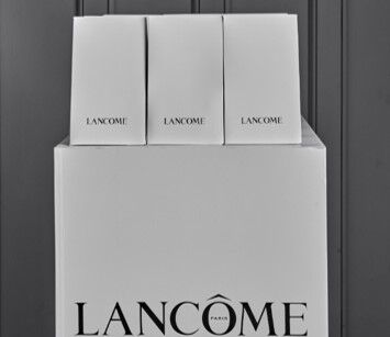 Cutii albe de produse Lancome, așezate pe un suport cu logo-ul Lancome.