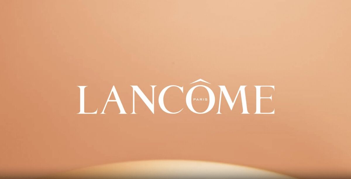Logo marki Lancôme na tle w odcieniu łososiowym.