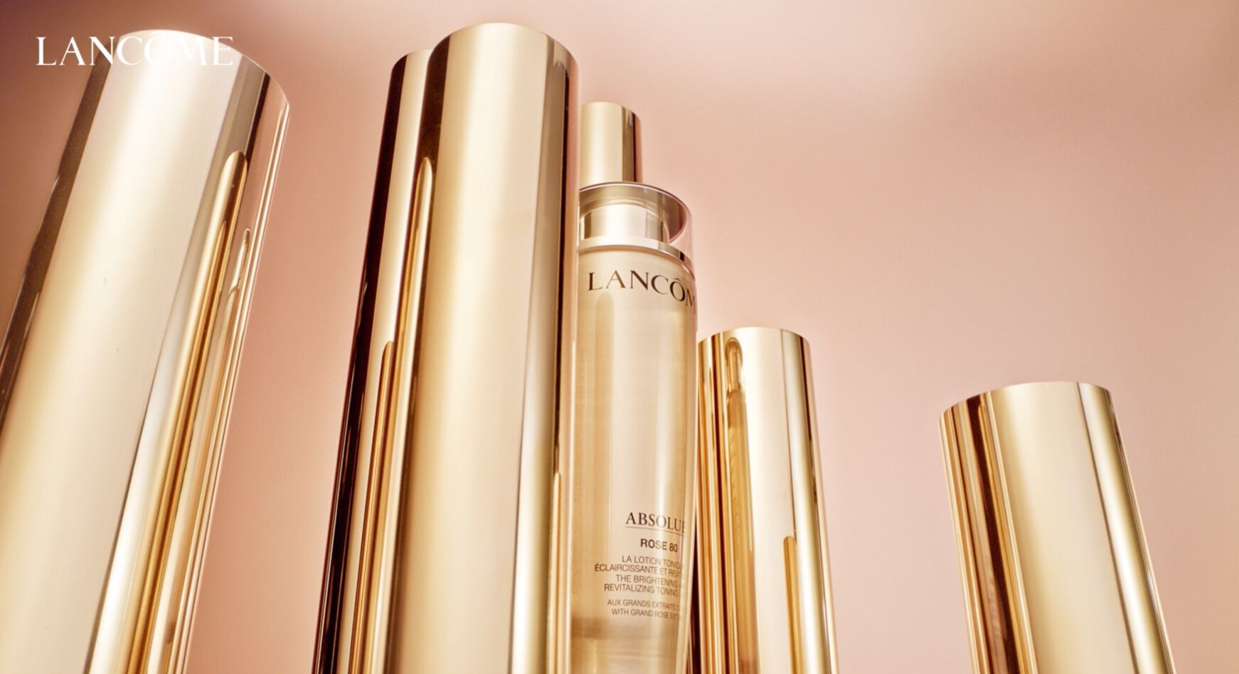Butelka serum Lancôme Absolue otoczona eleganckimi, złotymi opakowaniami w tle.